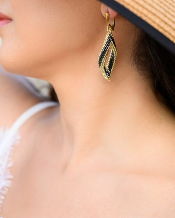 Close-up of a woman wearing Miyuki peyote earrings with a twisted design in gunmetal and gold tones